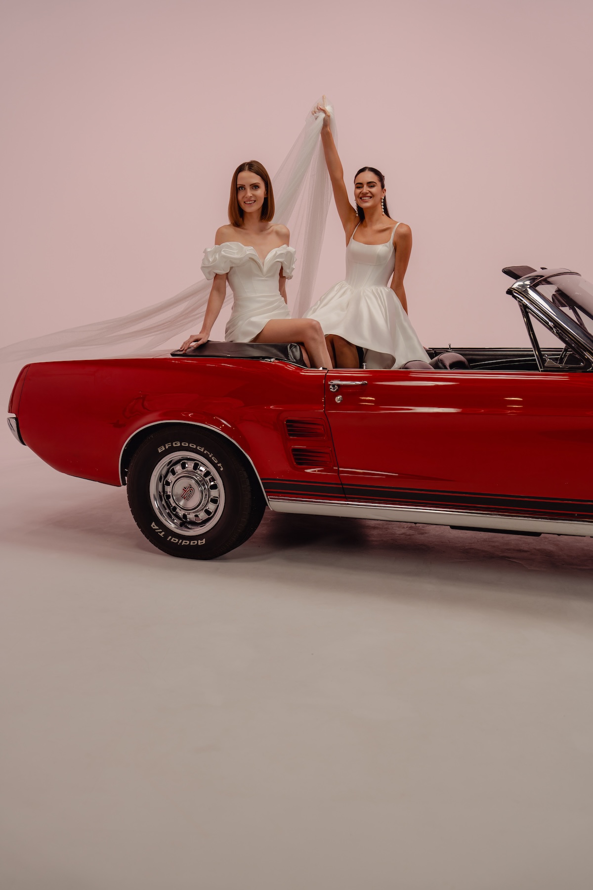 Shooting éditorial de robes de mariées civiles en location avec deux modèles dans une voiture vintage rouge