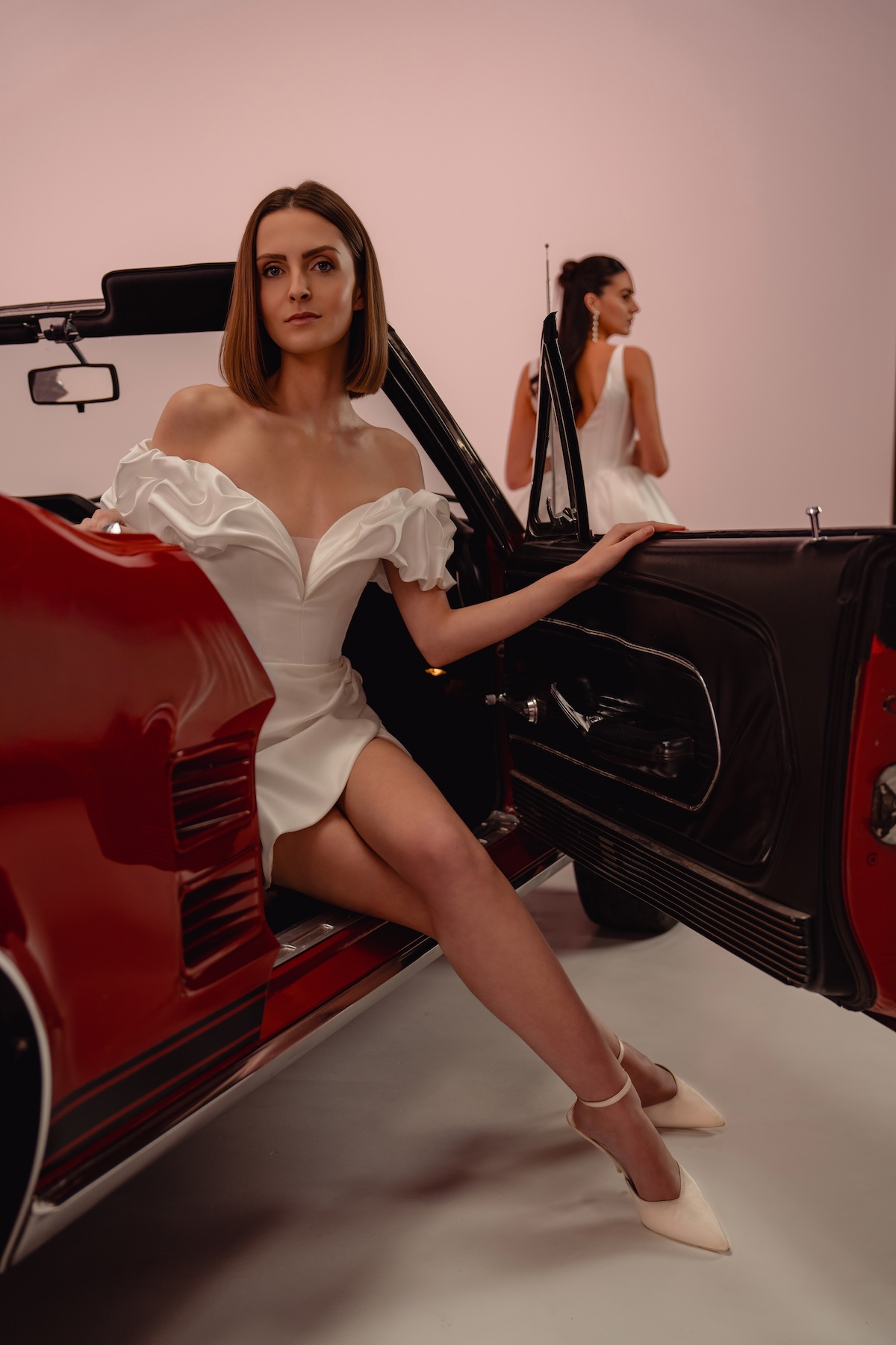 Velvet, robe de mariée civile courte en satin avec manches bouffantes, assise dans une voiture vintage rouge, en location à Toulouse