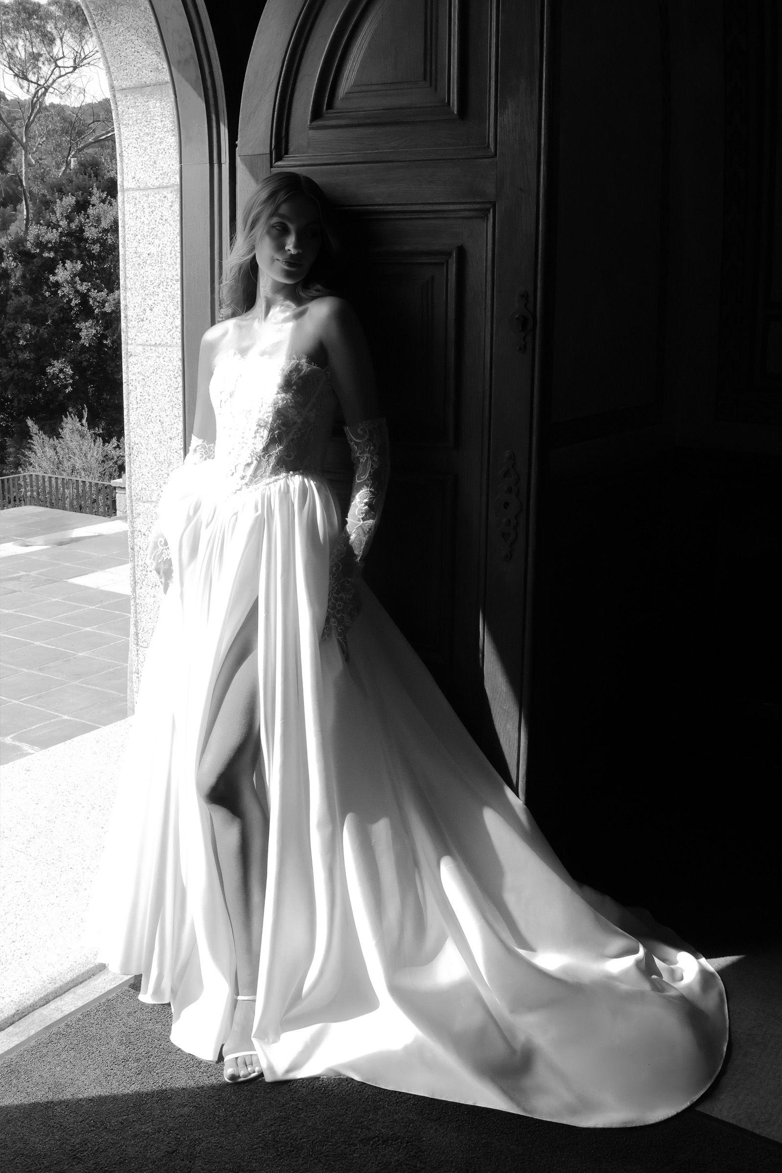 Robe de mariée bohème Léonie avec corset en dentelle florale, manches amovibles en dentelle et jupe fluide fendue photographiée entre ombre et lumière.