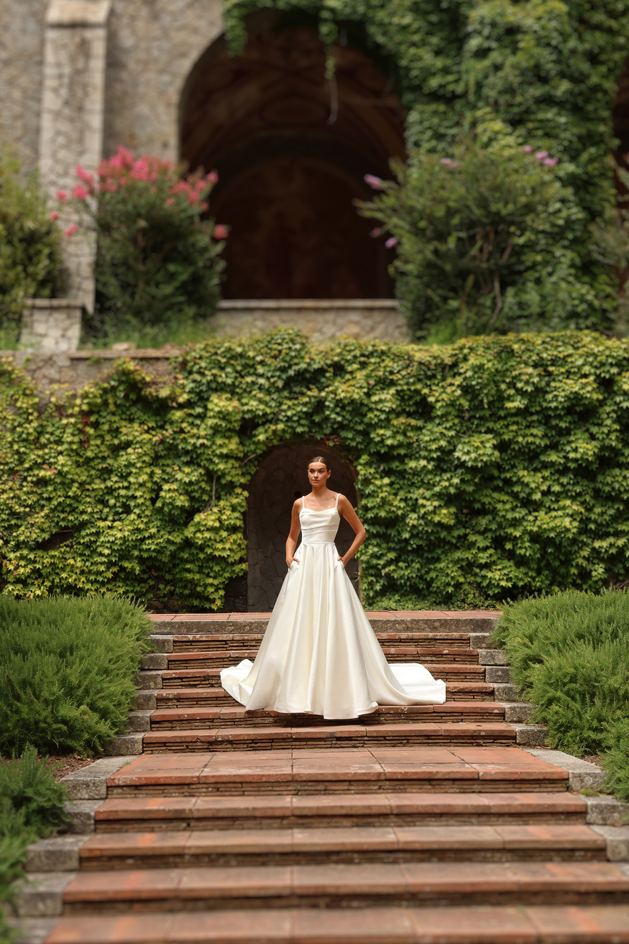 Robe de mariée moderne Apolline en crêpe avec longue traîne photographiée dans un jardin.