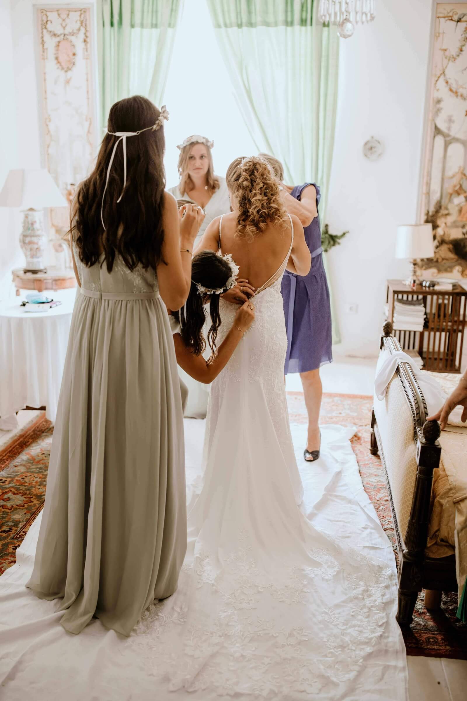 Sylvie entourée de ses proches pendant les préparatifs, sa robe de mariée et sa traîne vues de dos.