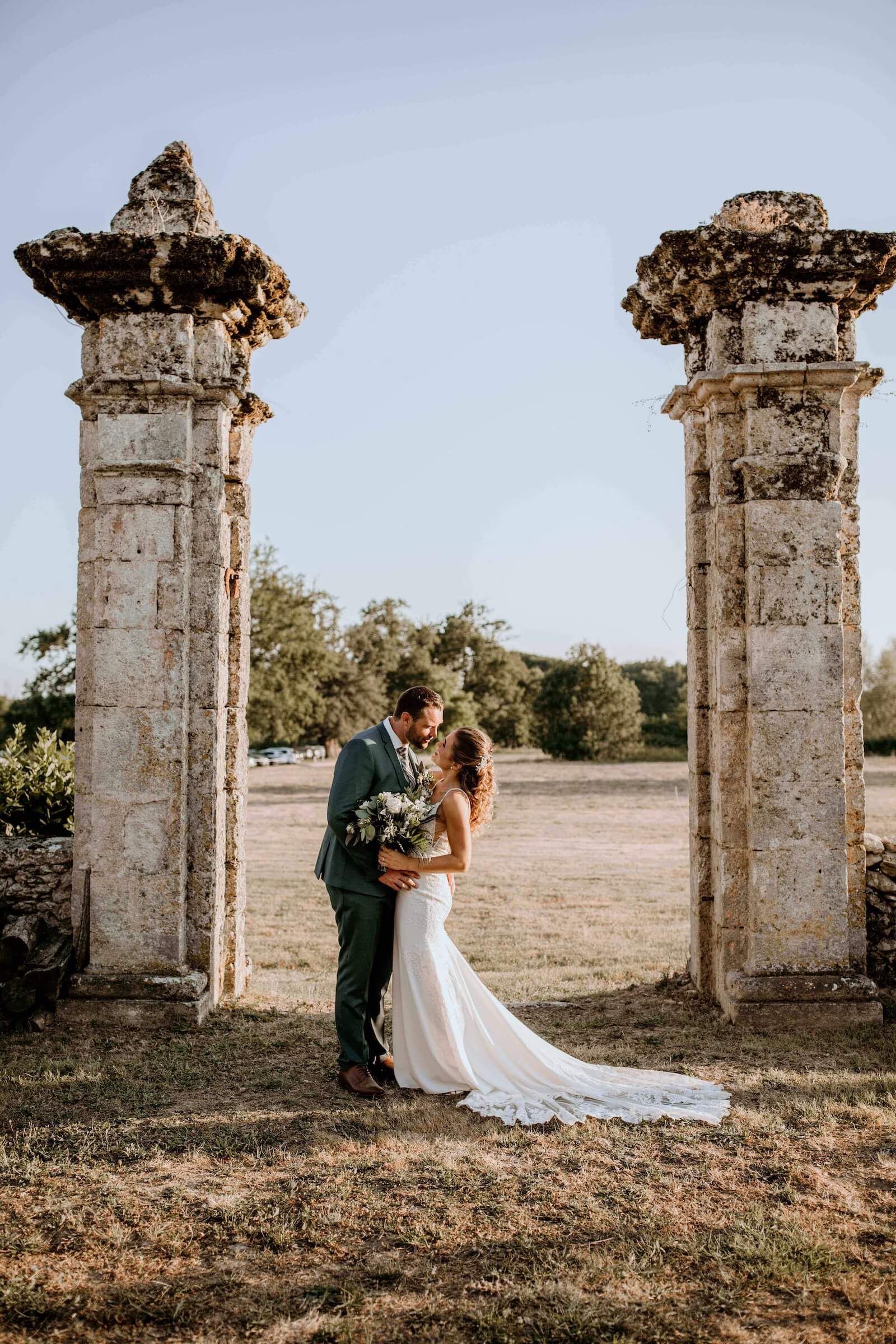 Sylvie et Julien souriants, photographiés de près, la mariée portant une robe en dentelle à fines bretelles.